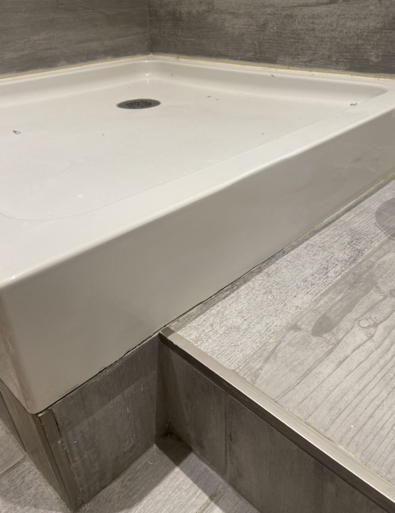 A white shower base with a raised lip sits in a tiled bathroom. The floor has a step.