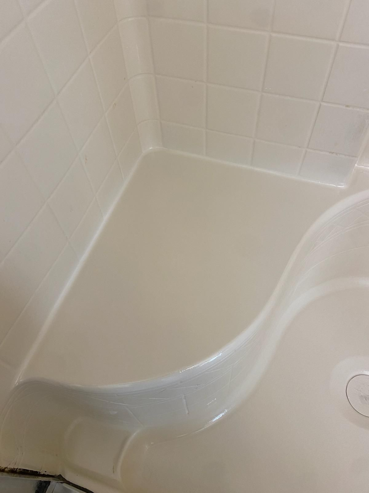 Off-white, accessible shower stall with built-in seat. Tiled walls and a smooth, sloped floor.