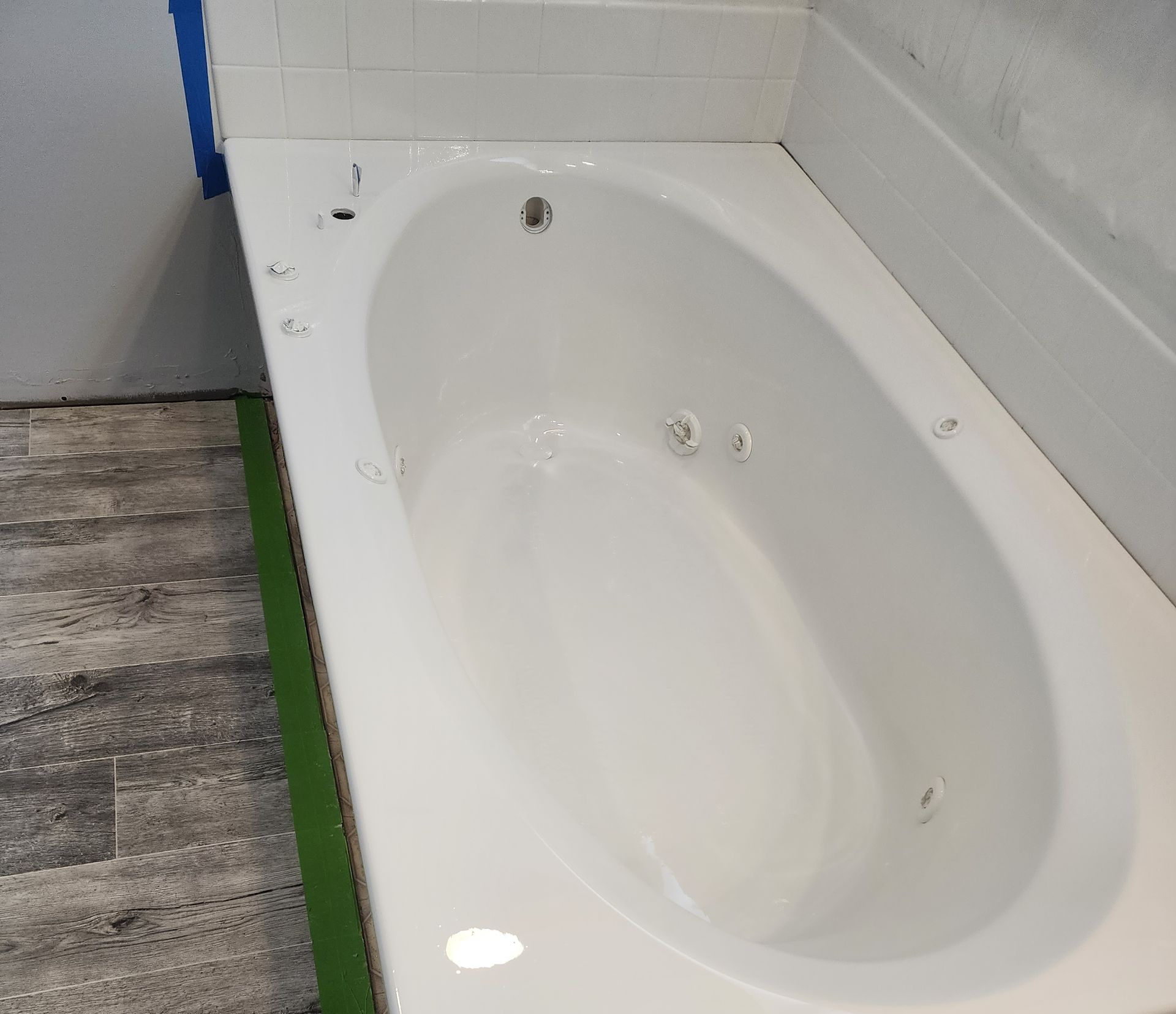 White oval bathtub with jets installed in a bathroom during renovation. Gray and white tile flooring.