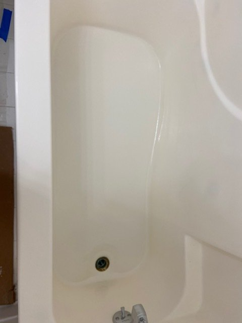 A cream-colored bathtub with a drain and a faucet. The tub is empty and clean, viewed from above.