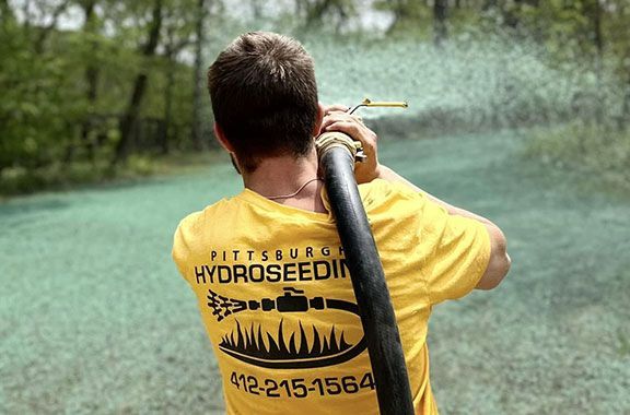 A man in a yellow shirt is spraying grass with a hose.