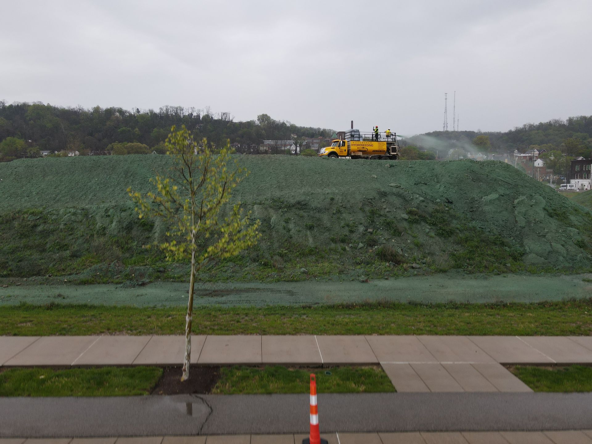 A large pile of grass is being sprayed on a hill.