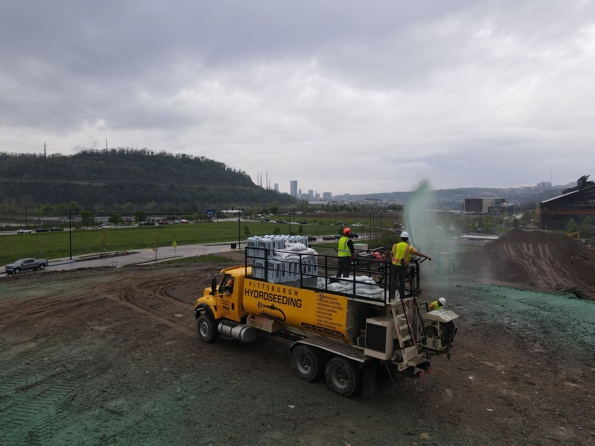 A yellow truck is spraying green grass on a dirt field.