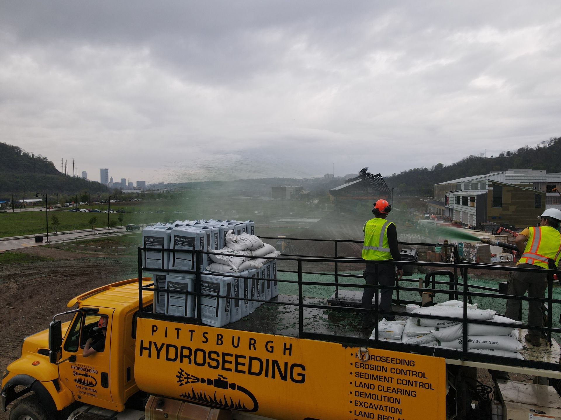 A yellow pittsburgh hydroseeding truck is being sprayed with water