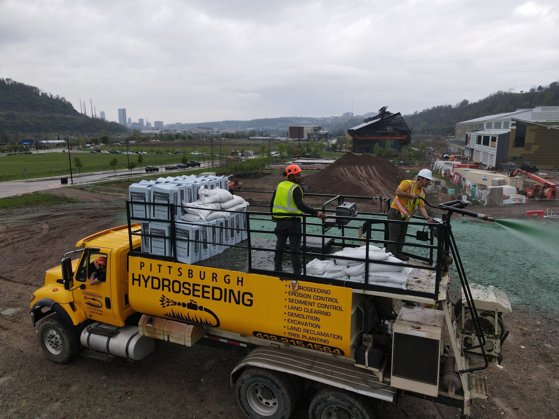 A yellow truck with the word hydroseeding on the side is being sprayed with water.