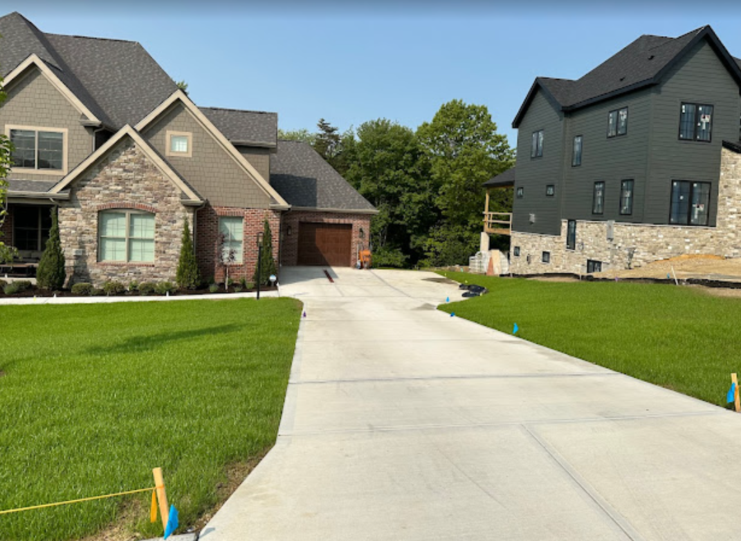 There is a concrete driveway leading to a large house.