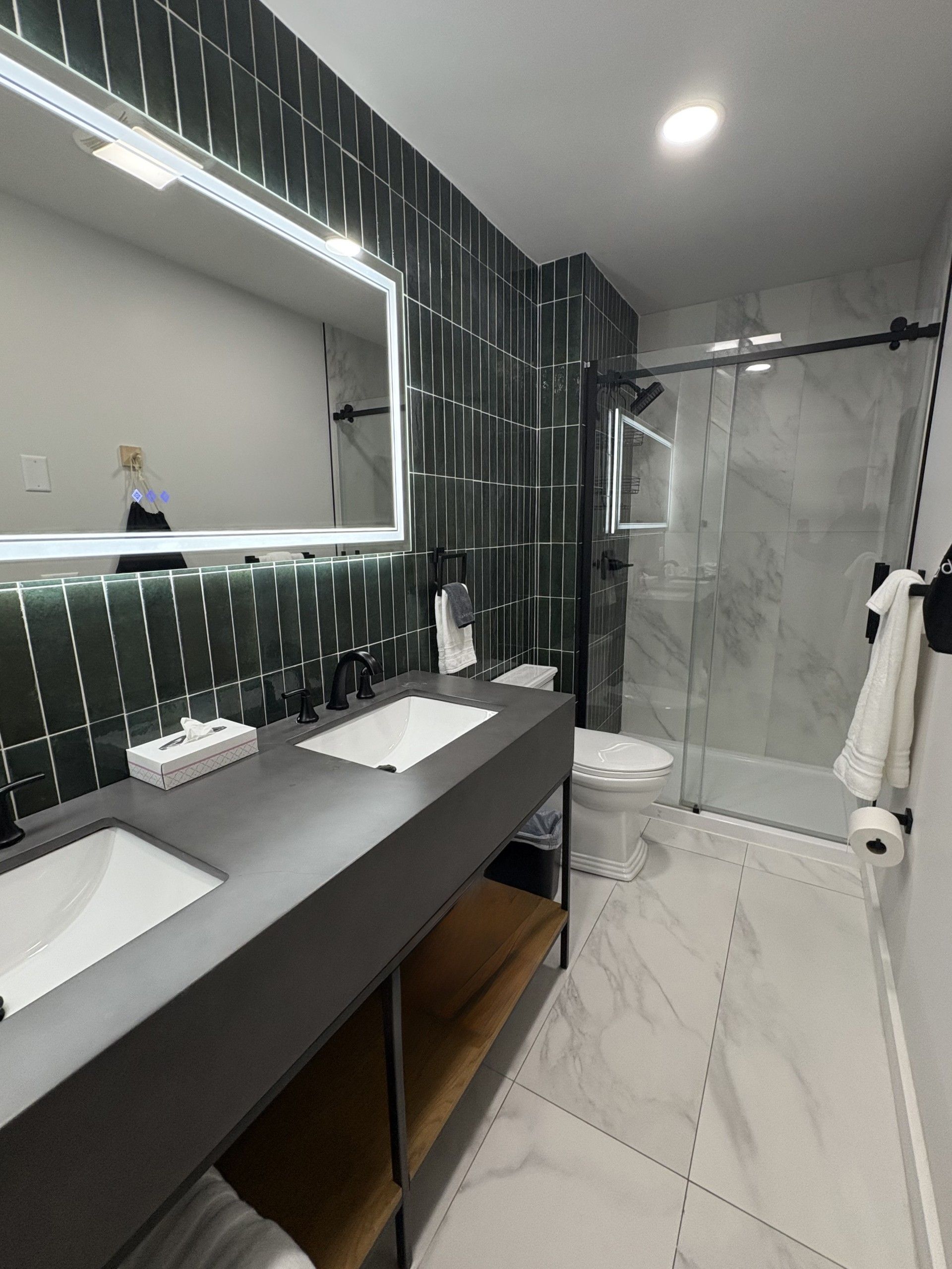 Modern bathroom with green tiled wall, double sink, and glass shower.