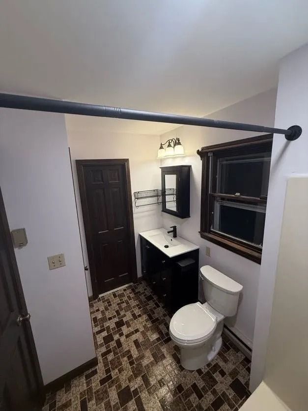 Bathroom with dark vanity, brown door, white toilet, and patterned tile floor.