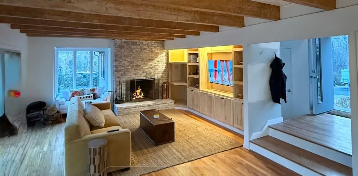 A cozy living room with a fireplace, wooden beams, built-in cabinets, and a rug.