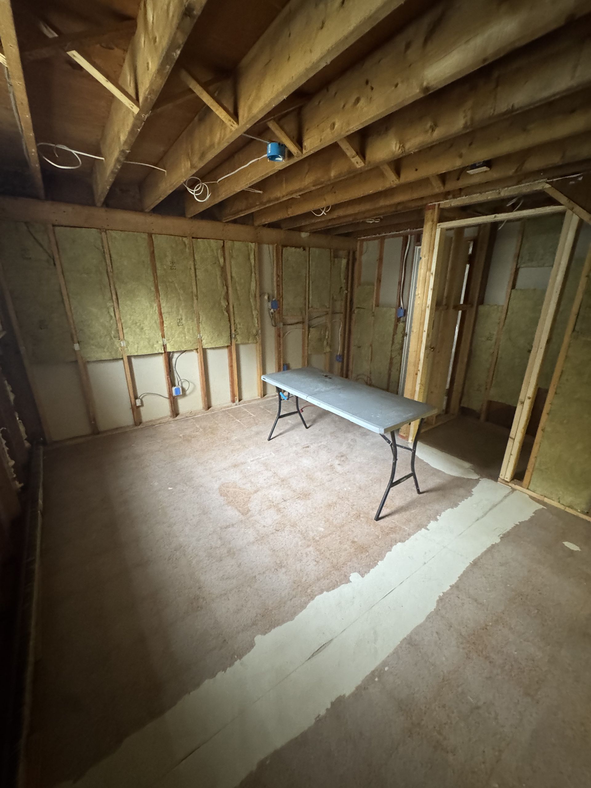 Interior of unfinished basement with insulation, exposed framing, and a folding table.