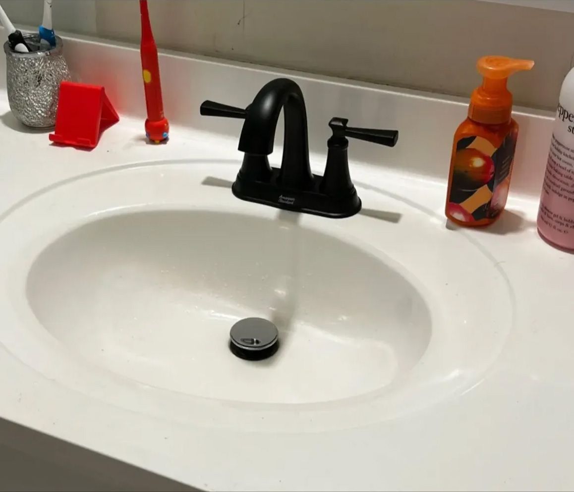 White bathroom sink with black faucet, soap, and toiletries.