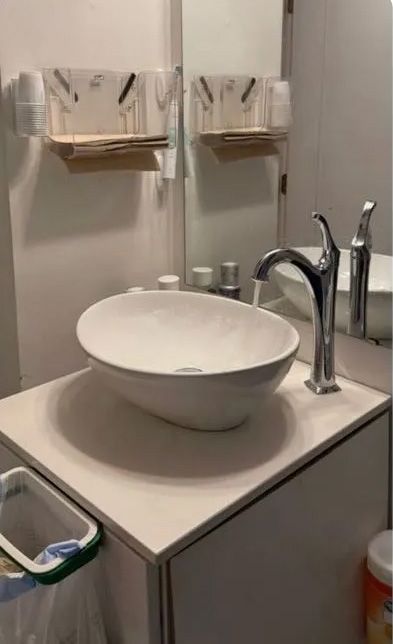 White oval sink on a white cabinet, chrome faucet, and a mirror in a bathroom setting.