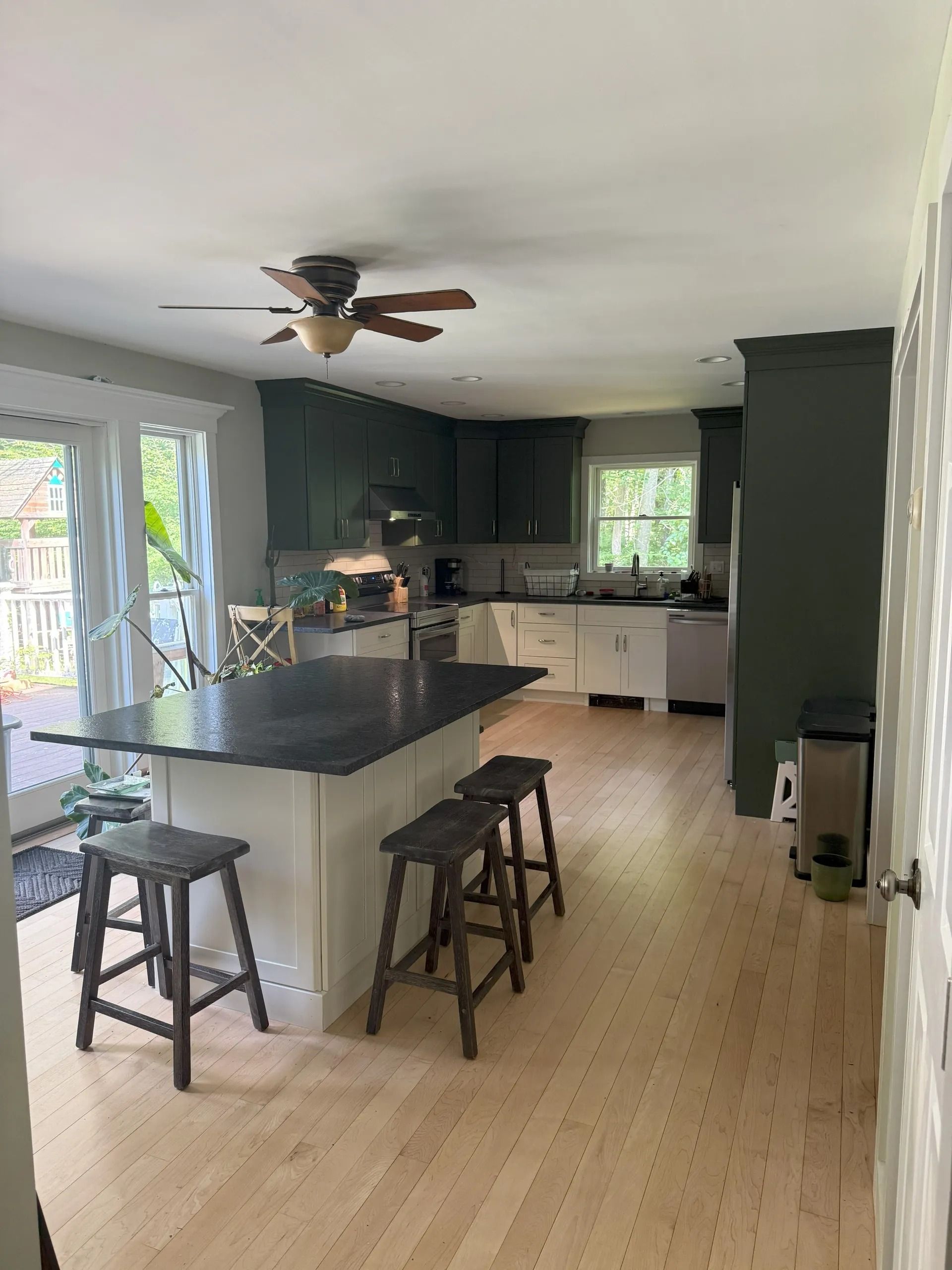 Kitchen with green cabinets, white island, black countertop, wood stools, and light wood flooring.