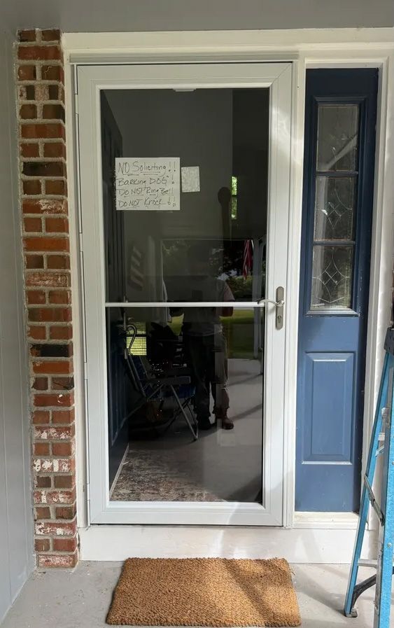 White screen door with a blue side door, brick accent, and a doormat.
