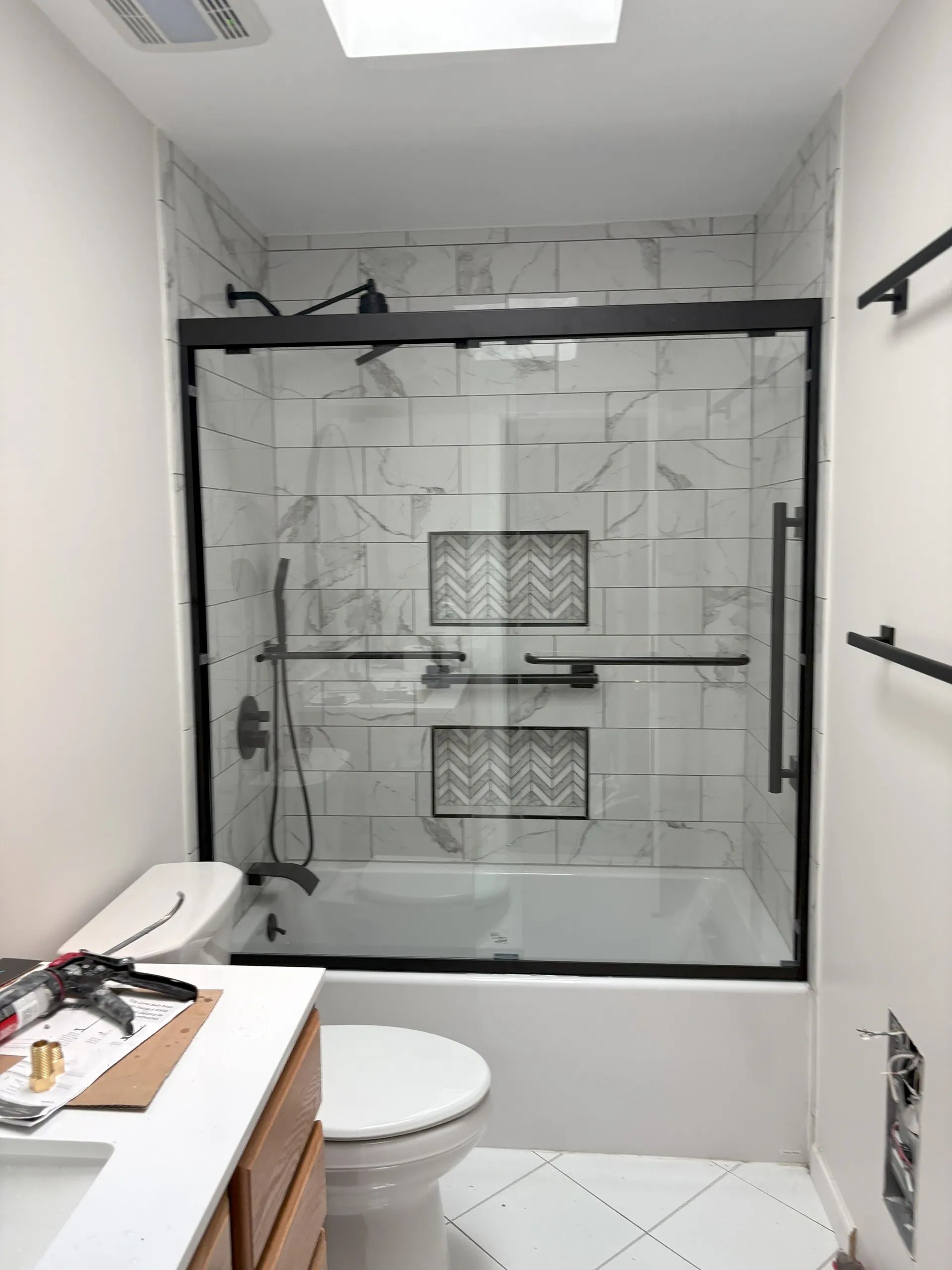 Bathroom with a tub and shower combo. White tile with black shower door frame.