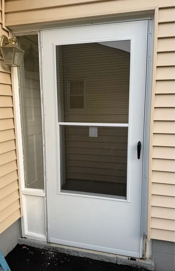 White screen door with a side panel on a beige building exterior.