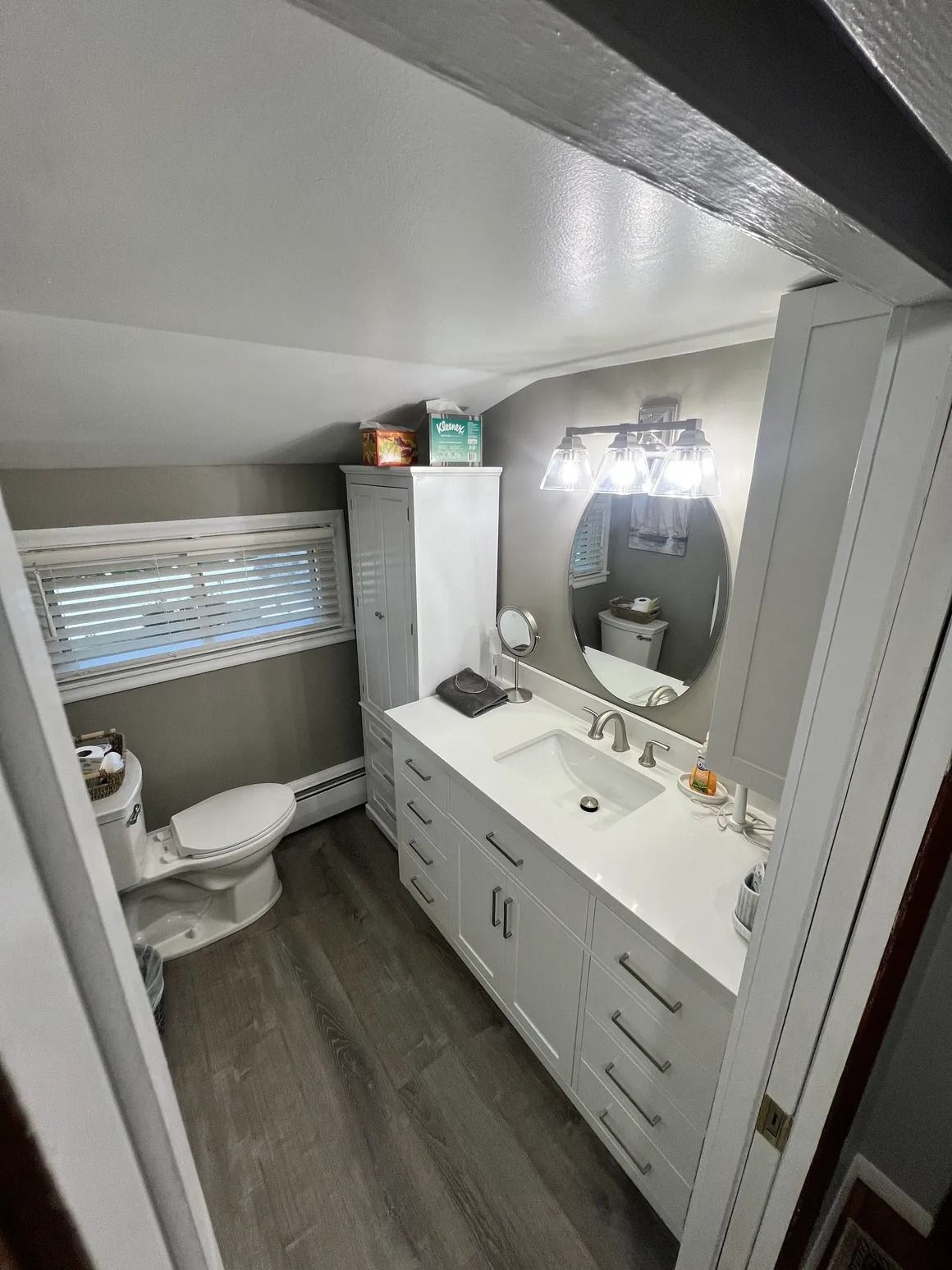 Bathroom with white cabinets, toilet, and a large mirror. Gray walls and flooring.