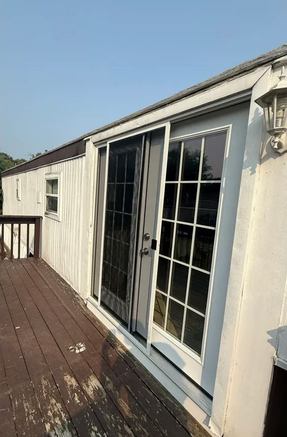Sliding glass door with screen on a wooden deck. White exterior wall and blue sky.