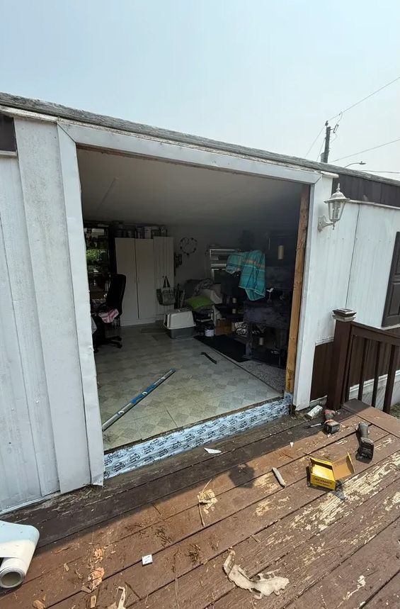 Open doorway of a mobile home. Overlooking a cluttered interior, visible from a weathered wooden deck.