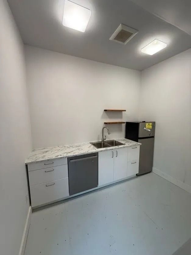Small kitchen with white cabinets, stainless steel sink, and refrigerator. Light gray floor and white walls.