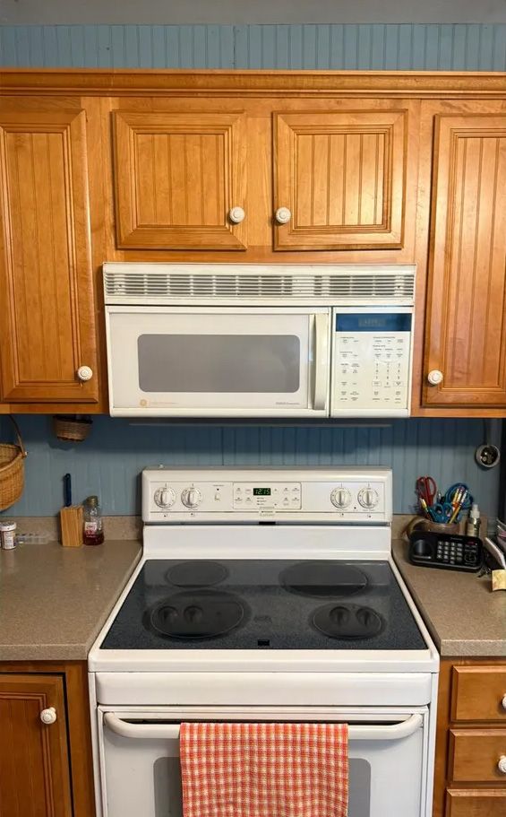 Kitchen with a white stove, built-in microwave, and light wood cabinets against a blue wall.