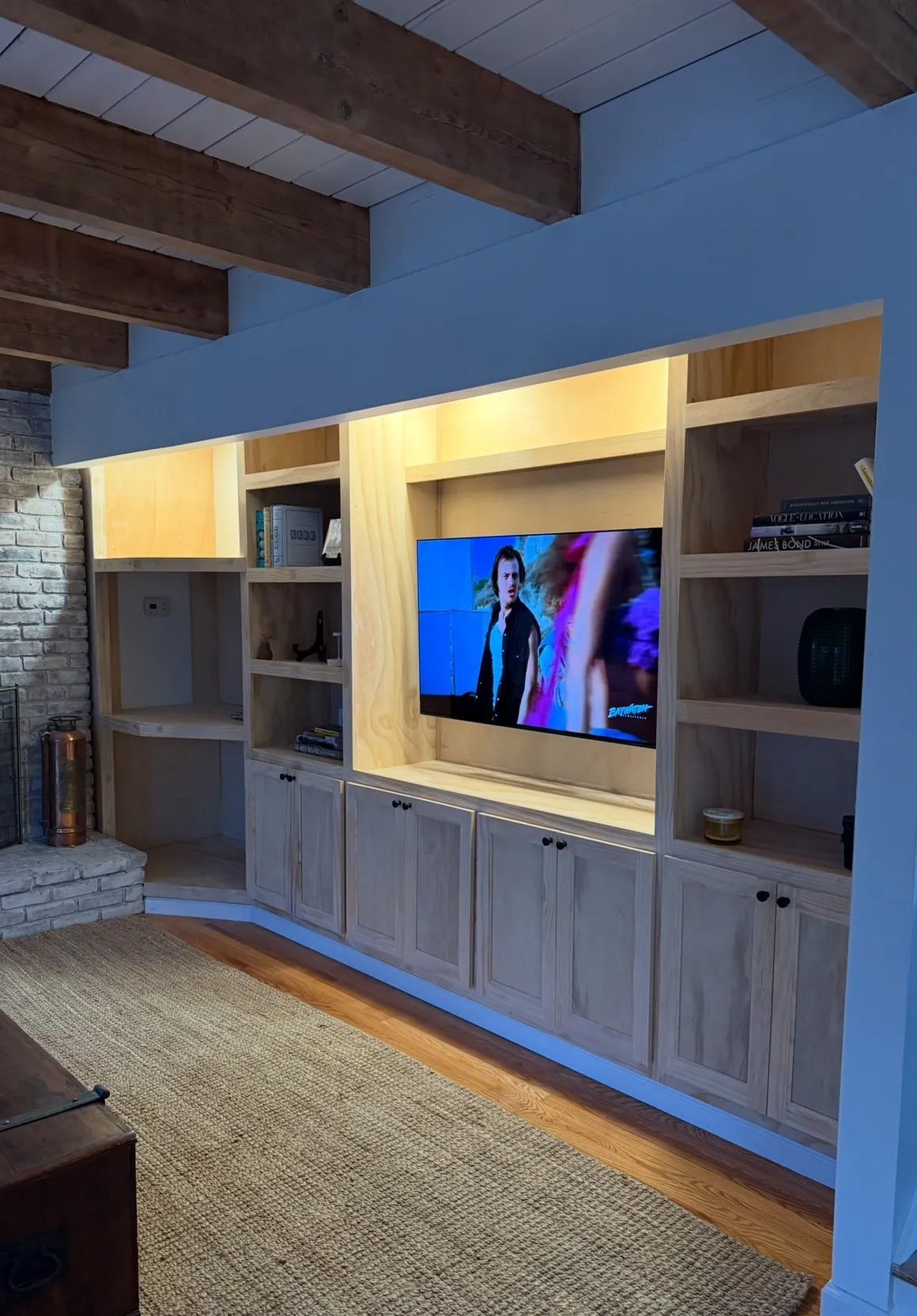 Built-in wooden entertainment center with TV, shelves, and cabinets against a light blue wall, in a room with a rug.
