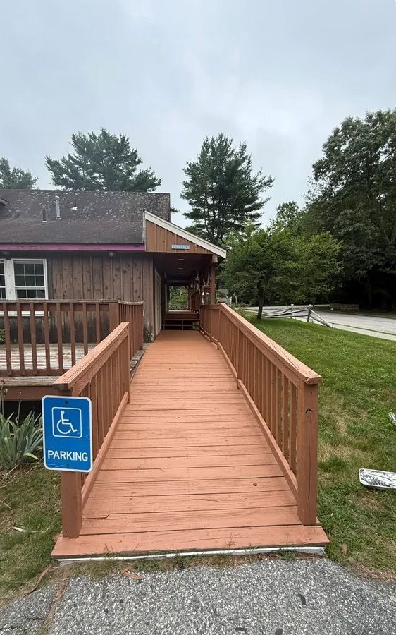 Wooden ramp leading to a building's entrance. Blue handicap parking sign is visible. Cloudy day.