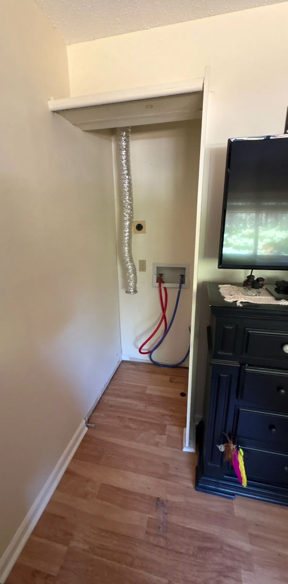 Laundry area with a dryer vent, water hookups, and a small opening in the wall. Brown laminate flooring.