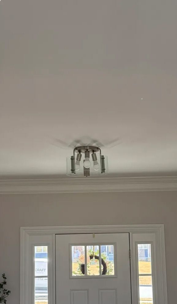 Ceiling light fixture above a white front door with sidelights. Silver light and white ceiling.