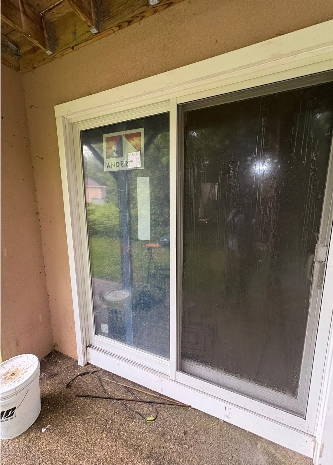 White-framed sliding glass door with a security shutter partially covering the left pane. Concrete patio, tan siding.