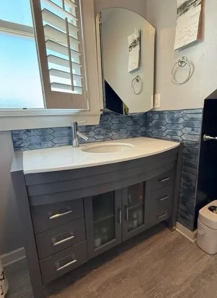 Gray bathroom vanity with white countertop, oval sink, large mirror, blue tile backsplash.