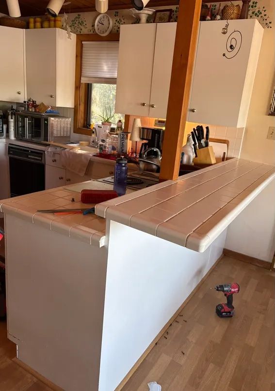 Kitchen renovation in progress, including a white countertop, cabinets, and a supporting beam. A drill sits on the floor.