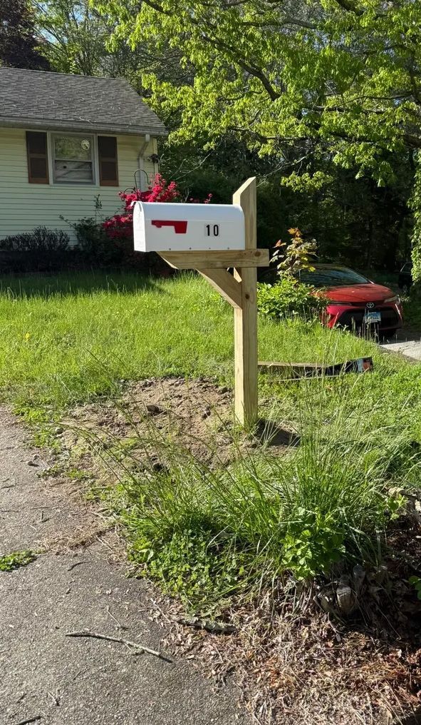 White mailbox with black address numbers on a wooden post in front of a house.