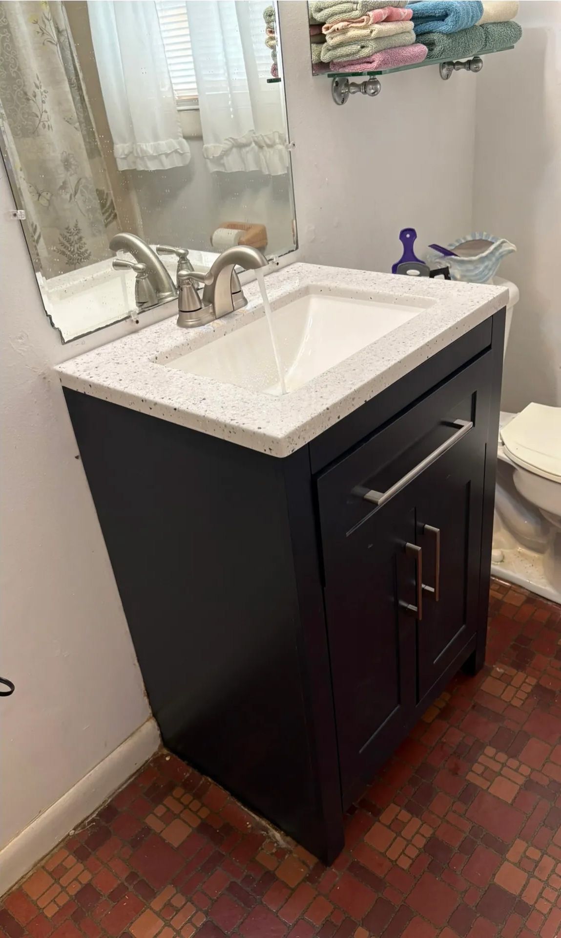Dark blue bathroom vanity with white speckled countertop, faucet running.
