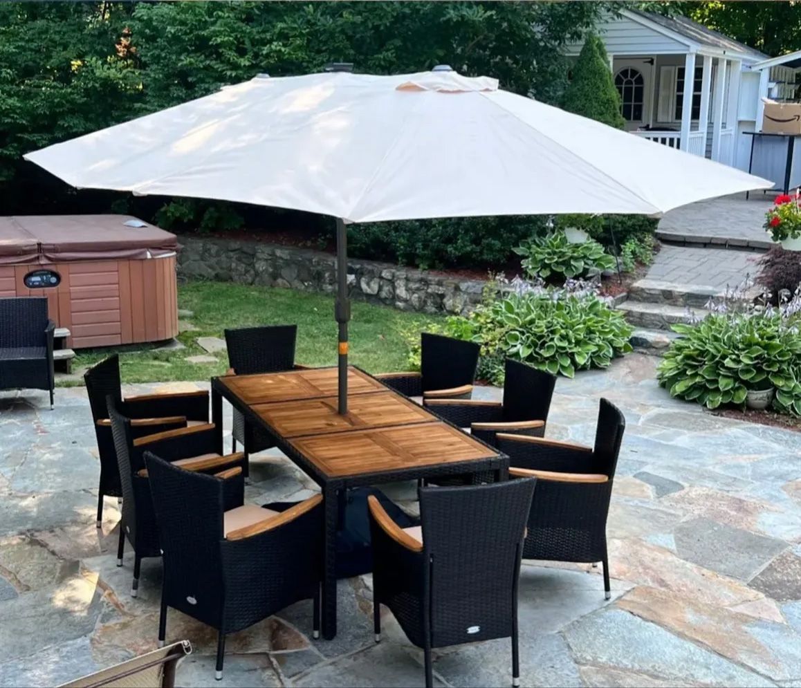 Outdoor dining set with umbrella; table, chairs, hot tub, and stone patio.