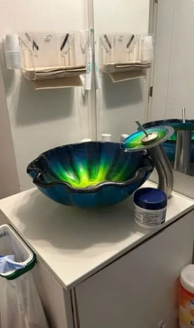 Bathroom sink with blue and green glass bowl, silver faucet, and white cabinet.