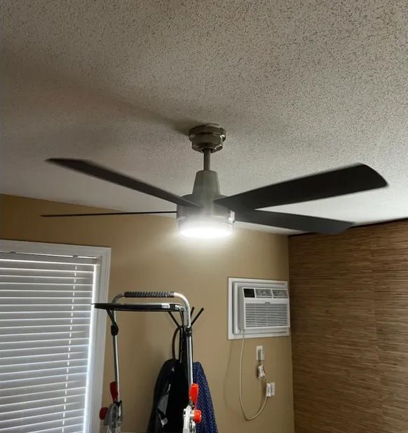 Ceiling fan with light on, spinning, in a room. Blinds and air conditioner are visible.