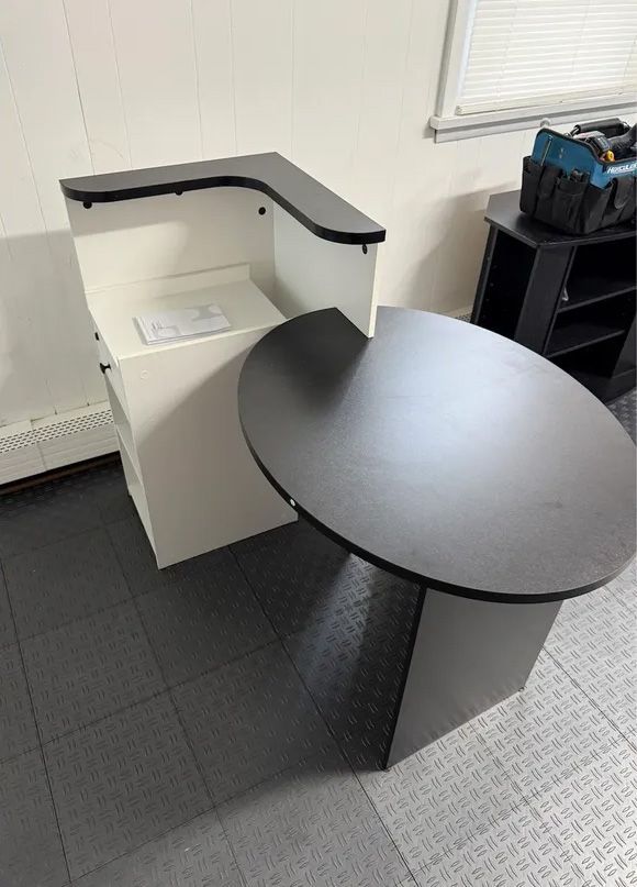 White and black office desk with a round black tabletop, set on a gray tiled floor.