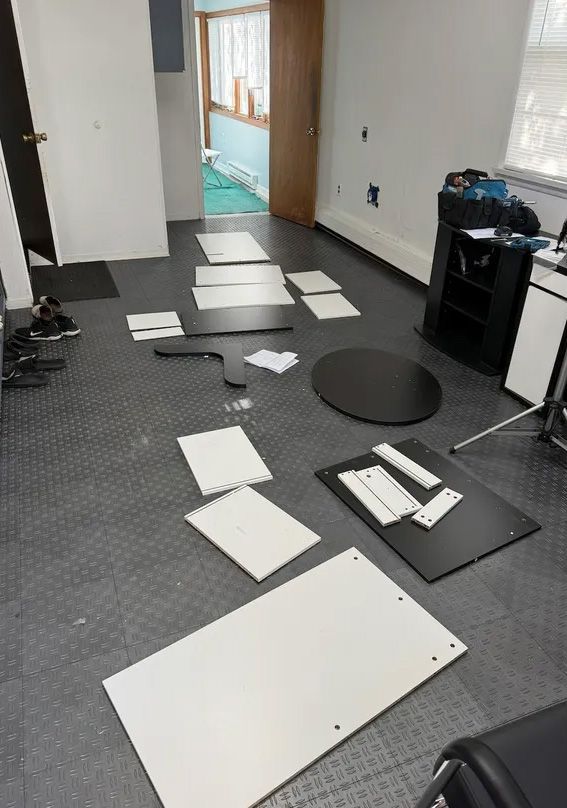 Disassembled black and white desk components spread across a dark floor in a room.