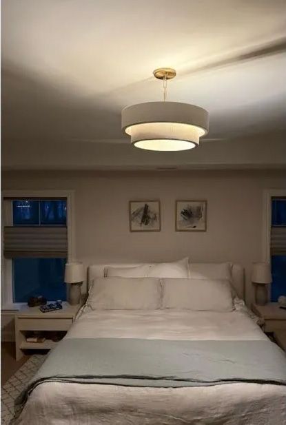 Bedroom with a layered white pendant light, bed with light blue throw, and two framed pictures above it.