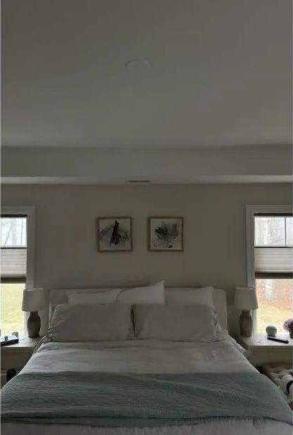 Bedroom with a white bed, neutral walls, two framed prints, and two windows.