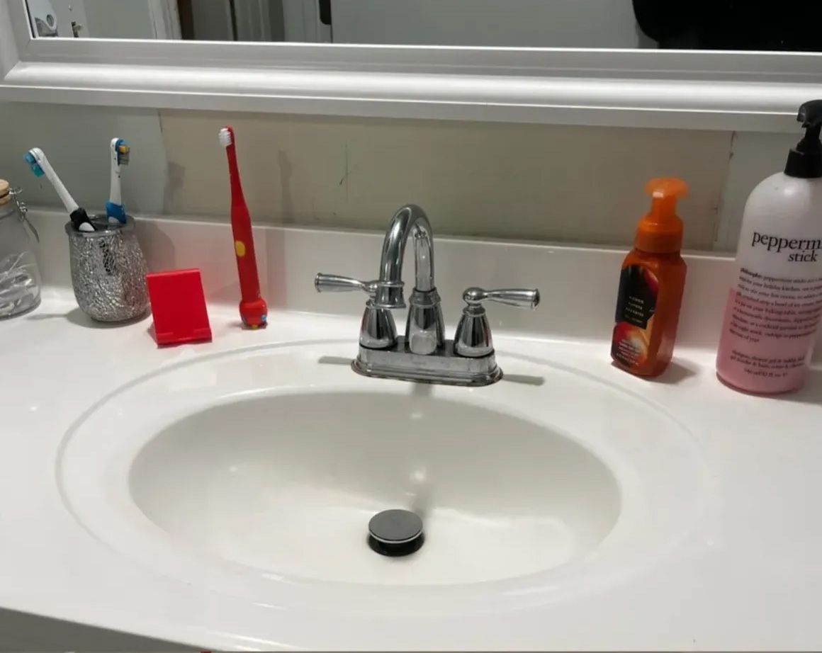 White bathroom sink with faucet, toiletries, and toothbrushes.