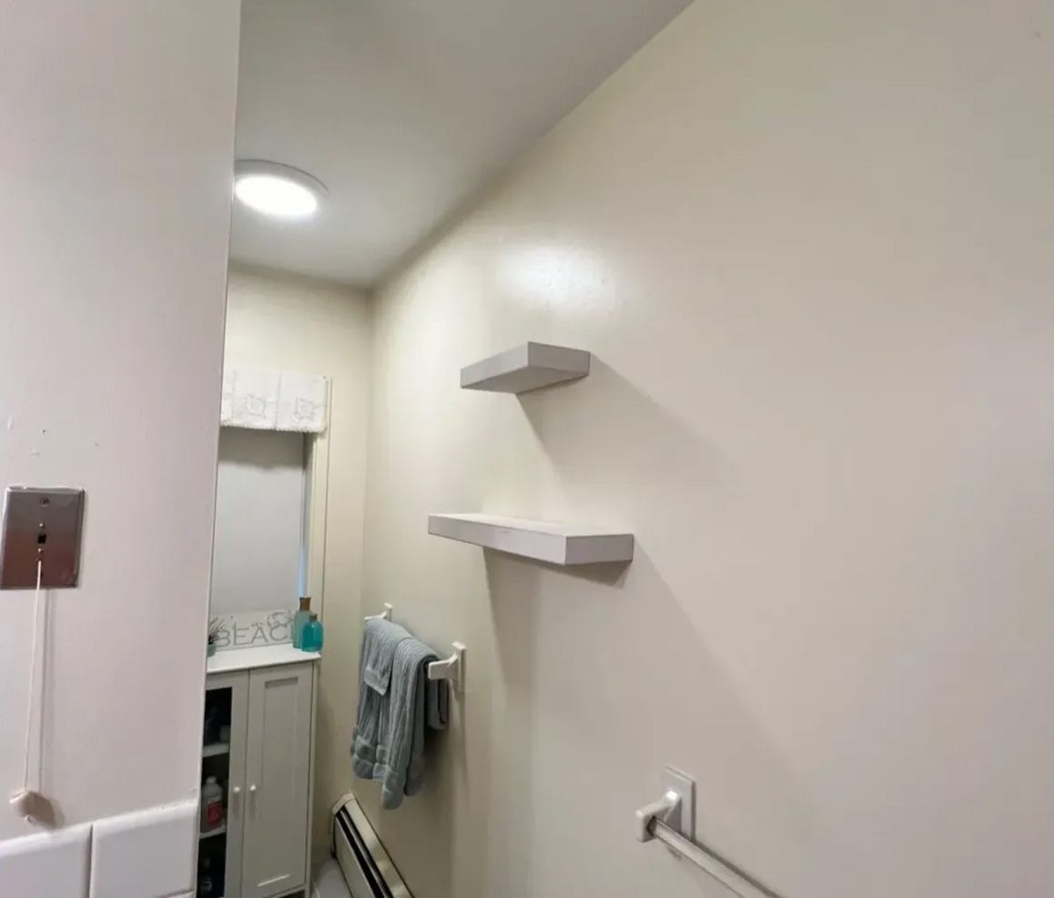 Bathroom interior with white walls, two floating shelves, and a towel rack.