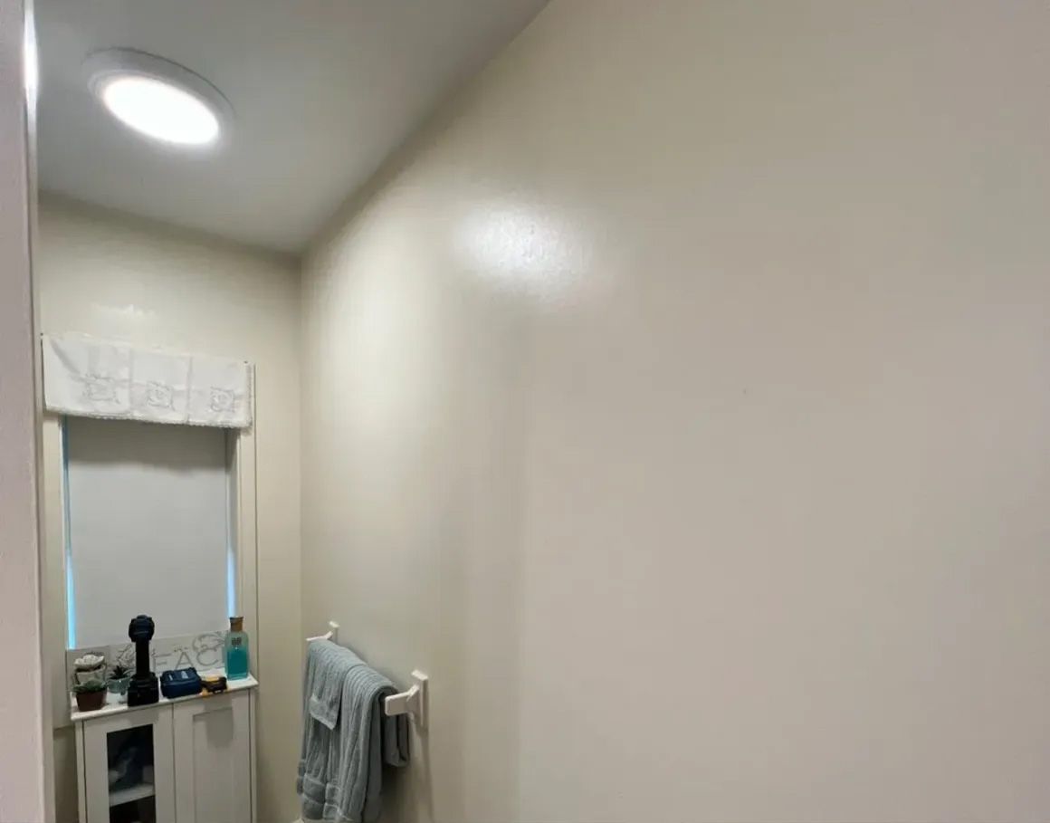 Bathroom interior with beige walls, a circular ceiling light, and a window with a cabinet below.