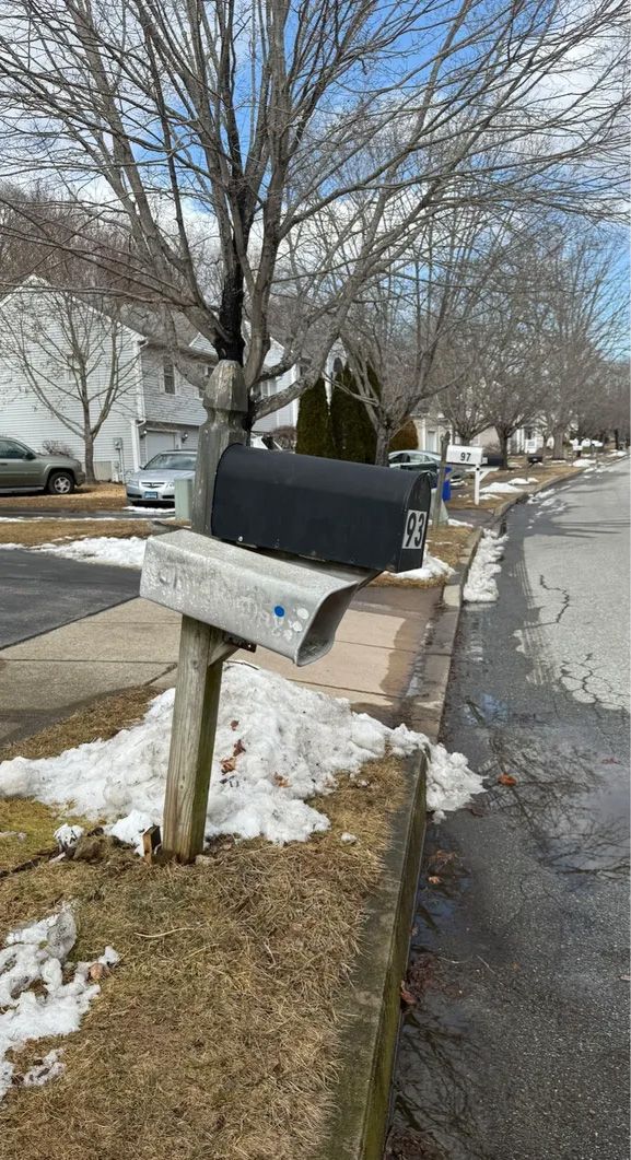 Black mailbox with partially melted snow on a curb beside a road.