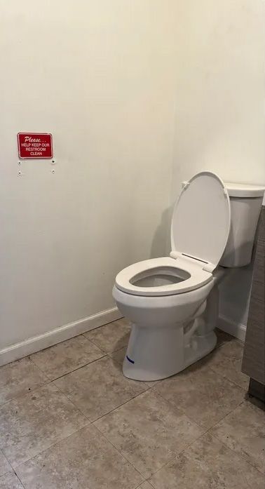 Toilet in a small bathroom with open lid. Red sign on the wall to the left.