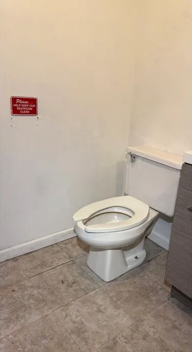 Toilet in a small bathroom with beige tile floor and a red sign on the wall.