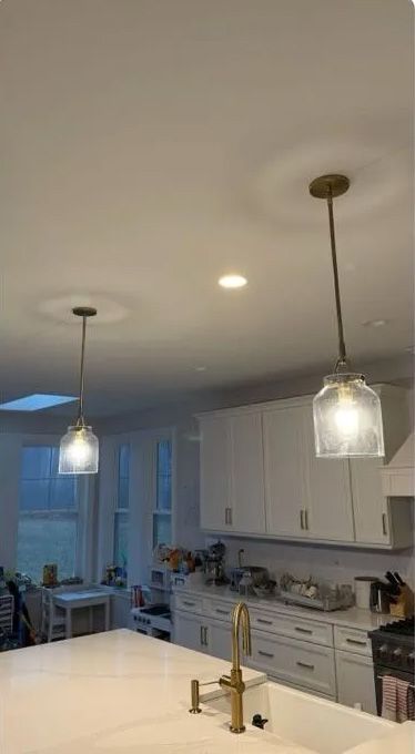 Two pendant lights hang above a white kitchen island. White cabinets and a window are in the background.