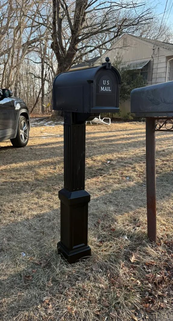 Black mailbox on a black post in a grassy area, another mailbox to the right, and a car to the left.