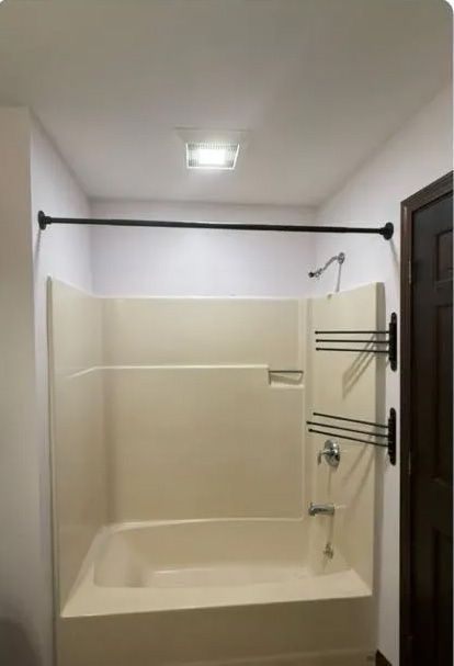 Bathroom with beige bathtub/shower, black shower rod, and towel rack on the wall.
